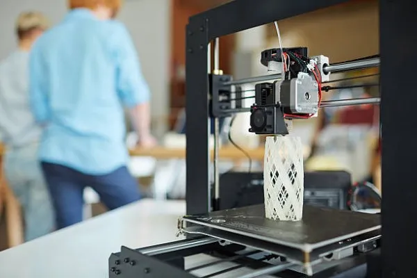 Tipos de impresión 3D; impresora 3D en medio de un trabajo con dos especialistas en diseño de fondo