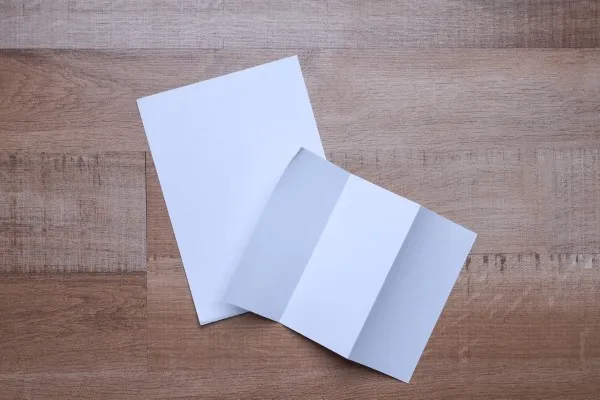 Dos flyers en blanco, uno desplegado y otro completamente extendido, reposan sobre una superficie de madera listos para personalizarse.