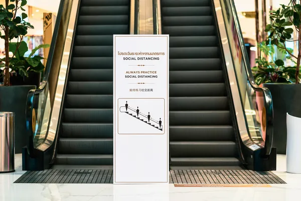 Foto de un banner roll up blanco entre dos escaleras eléctricas en un centro comercial de día.