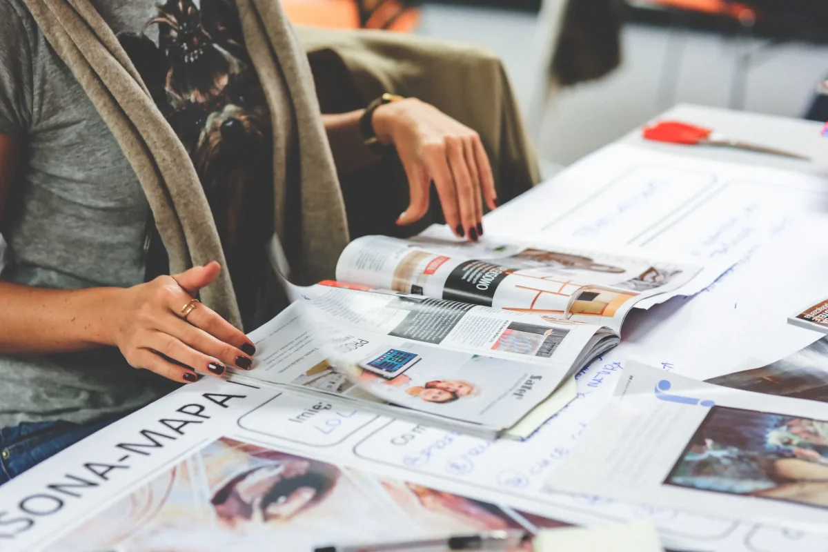 Una persona revisa un tabloide abierto sobre una mesa, observando diferentes artículos y fotografías dispuestos en formato editorial.