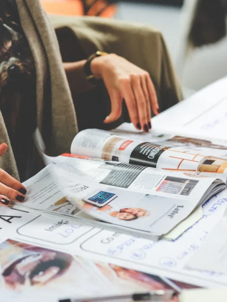 Una persona revisa un tabloide abierto sobre una mesa, observando diferentes artículos y fotografías dispuestos en formato editorial.