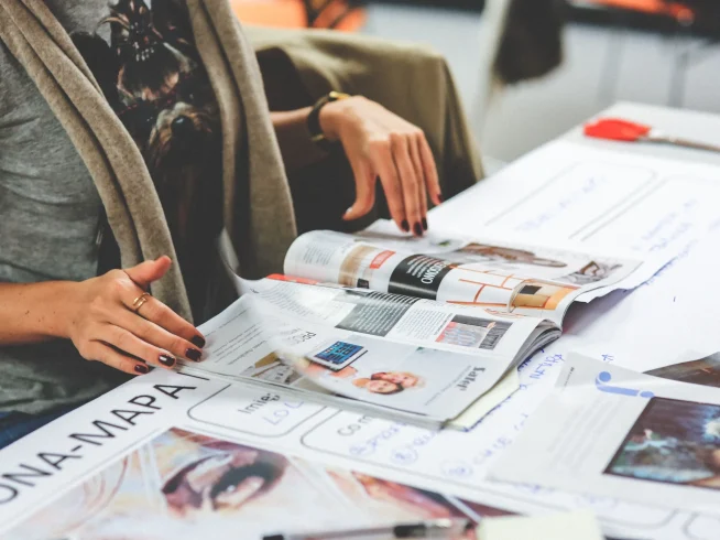 Una persona revisa un tabloide abierto sobre una mesa, observando diferentes artículos y fotografías dispuestos en formato editorial.